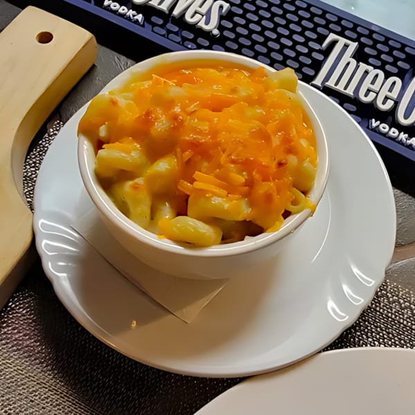 A white bowl of Jamaican mac and cheese with melted orange cheese, on a white plate.