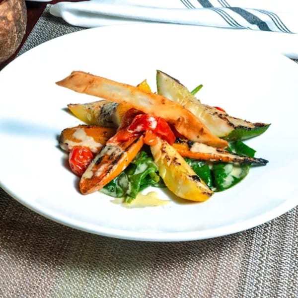 Grilled vegetables including zucchini, carrots, and tomatoes on a bed of spinach with a light sauce.