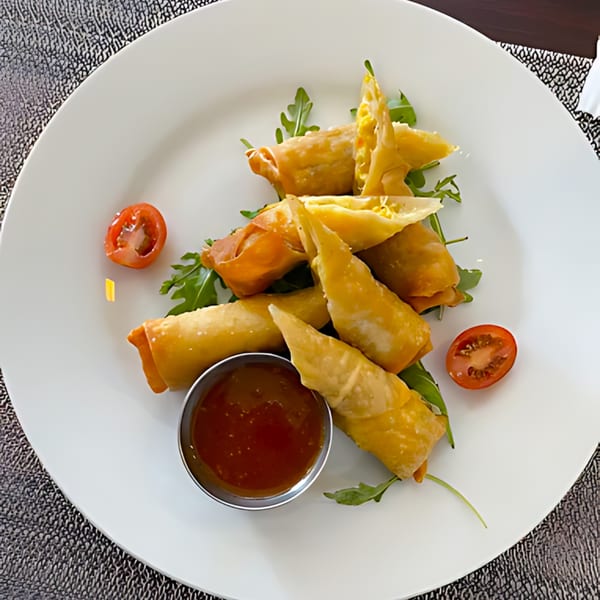 Crispy Jamaican spring rolls with a sweet chili dipping sauce, arugula, and cherry tomatoes.