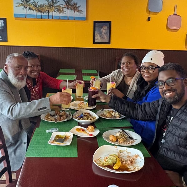 Six happy diners at Trelawny Fusion Kitchen toasting drinks around a table of Jamaican food.