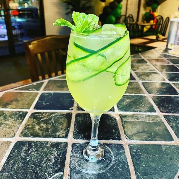 A refreshing green cocktail with cucumber slices and basil garnish sits on a tiled table at Trelawny Fusion Kitchen.