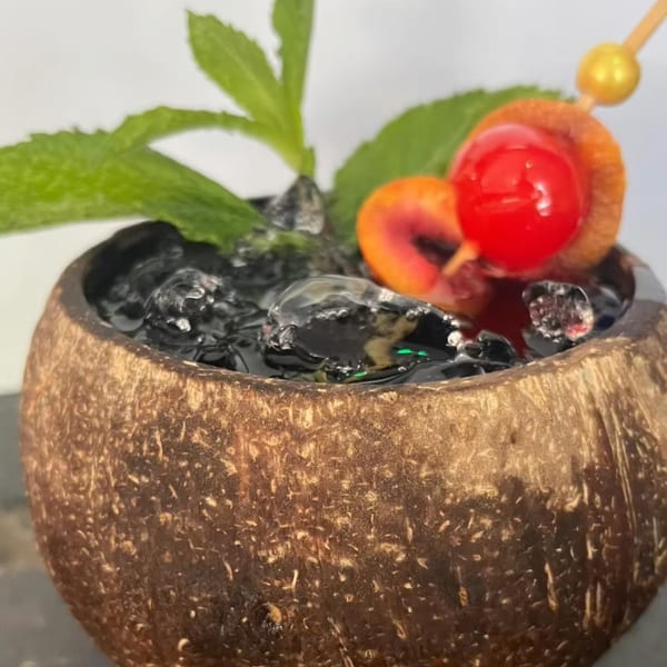 A Jamaican cocktail in a coconut shell, garnished with mint, cherry, and orange peel.